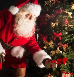 Santa Claus putting Christmas gifts by a tree.