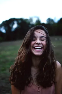 A girl smiling, eyes closed, against an outdoor scene