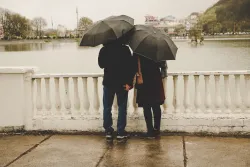 A couple standing on a bridge with umbrellas