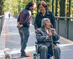 a woman pushing an older woman in a wheelchair while another woman watches