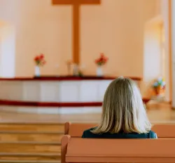 A woman sitting in church looking toward the alter and cross.