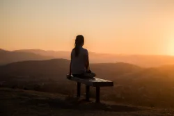 A woman sitting on a bench watching the sunset.