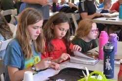 three little girls seated at a table with an open Bible and notebook