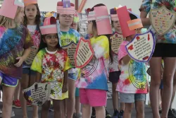 children in tie-dye shirts wearing paper helmets and pretend shields