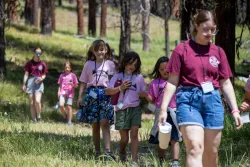 a line of girls walking through the grass and wearing matching pink shirts