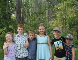 six children standing in a line with arms around one another's shoulders outdoors