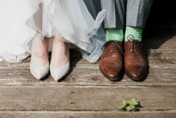 two pairs of feet, one wearing bridal shoes, one wearing men's dress shoes
