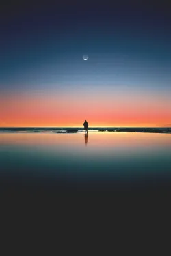 A calming image of a man silhouetted against a serene sunset on the beach