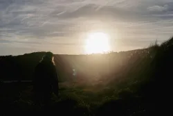 A bright sunset going down over a hill with a person in the foreground.