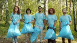 five people wearing matching blue shirts and holding garbage bags while standing outside