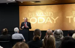 a man speaking to a crowd in front of a Beyond Today banner