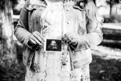 A woman holding up an ultrasound image of a baby in front of her belly.