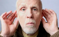 An older man cups his ear, illustrating the God-designed shape of the outer ear that amplifies sound—reminding us that even hearing reflects intelligent design.