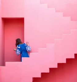 a woman looking through a doorway in the midst of two pink staircases