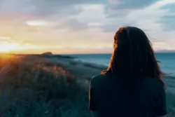 A woman looking off in the distance with the sun setting. 