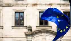 A European Flag blowing in the wind outside of an old building.