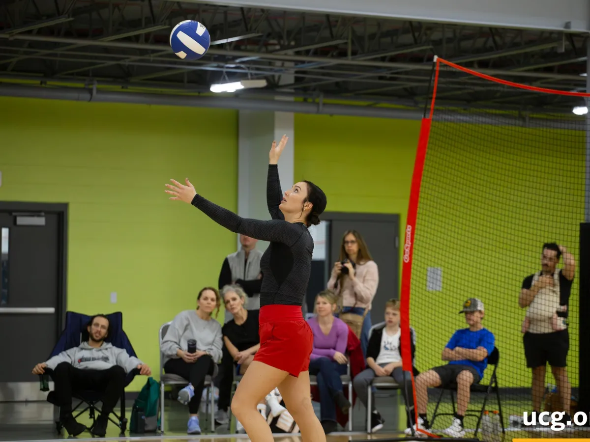 a woman throwing a volleyball indoors with a group of people watching