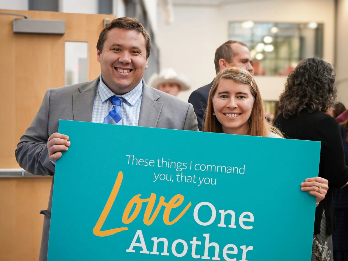 a man and a woman holding a "love one another" sign