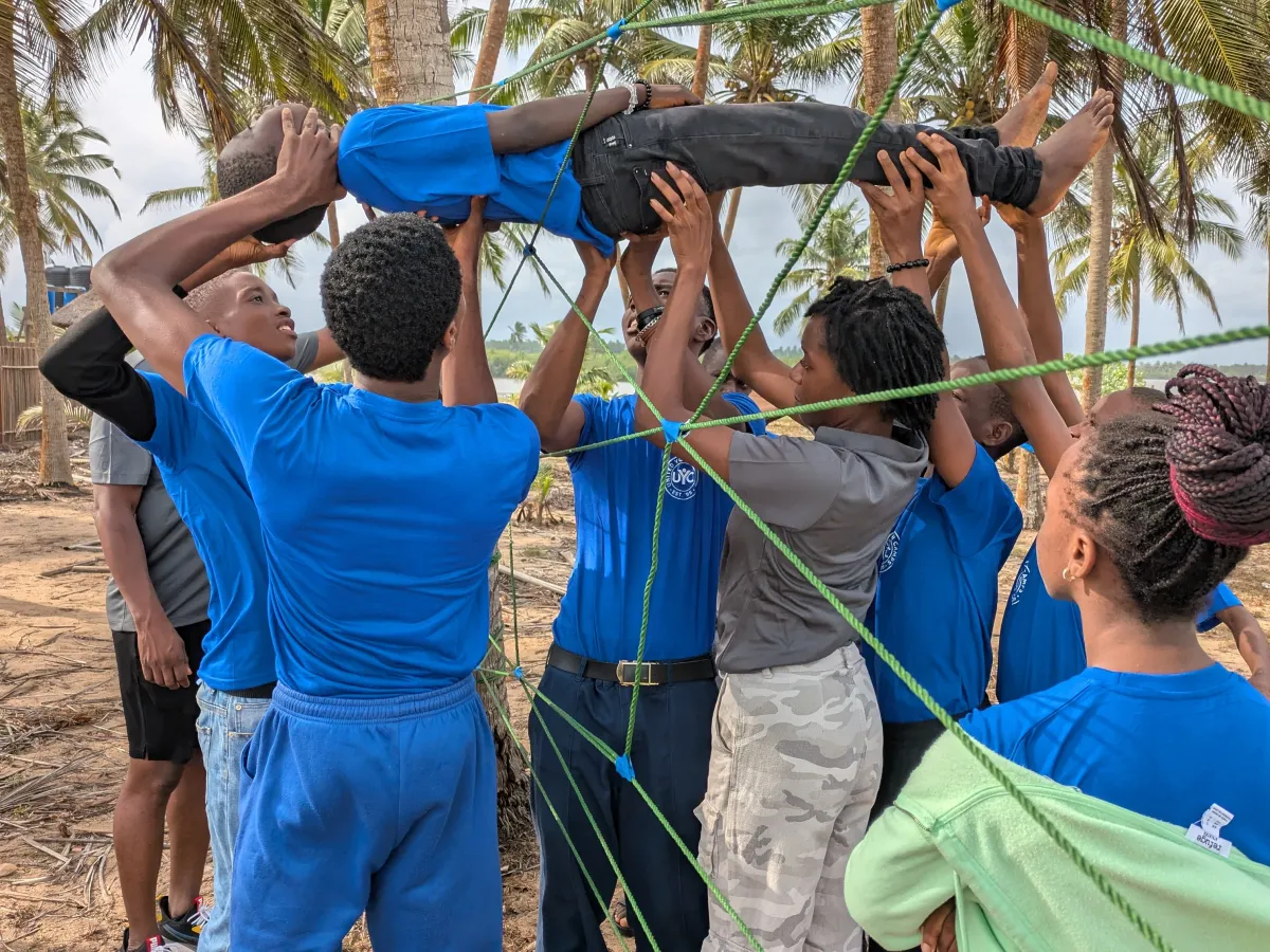 a group of teenagers lifting a boy through a web of rope