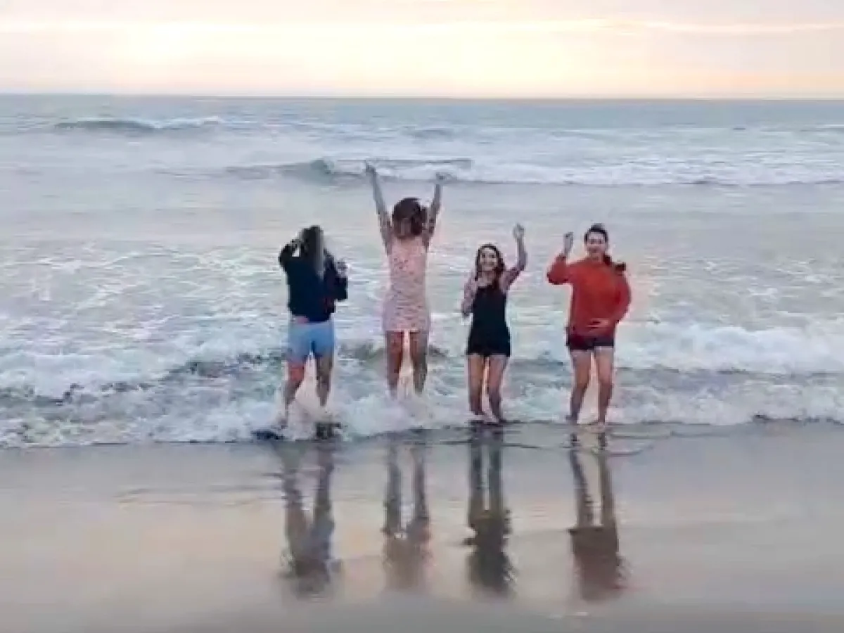 four teenagers on the beach at the water's edge