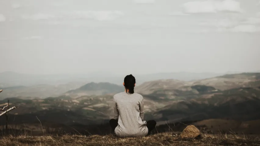 A woman sitting beside herself looking at the view of mountains.